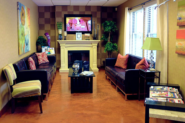 Comfortable waiting room at Nelson Vein Clinic in Cleveland, Ohio featuring cozy sofas, coffee table, fireplace, television, lamp and elegant decorations. Natural light floods through large windows with blinds. Sophisticated touch with Nelson magazines on the side table.