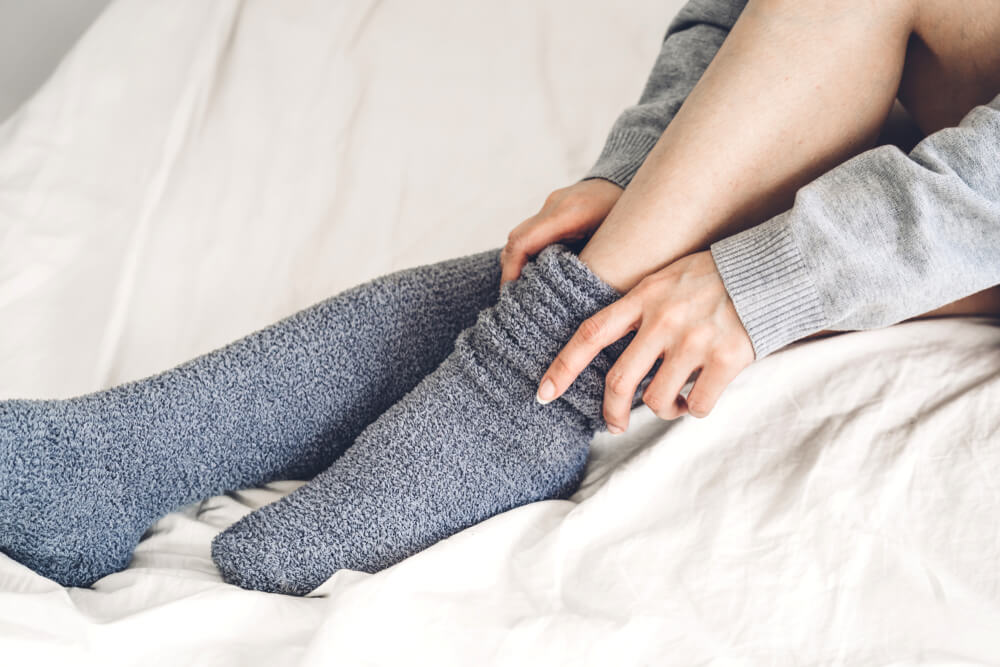 A woman putting on socks to combat cold weather.