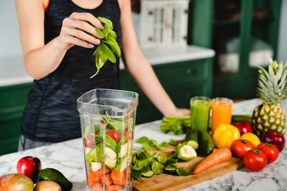 A woman putting healthy vegetables and fruits in a blender.