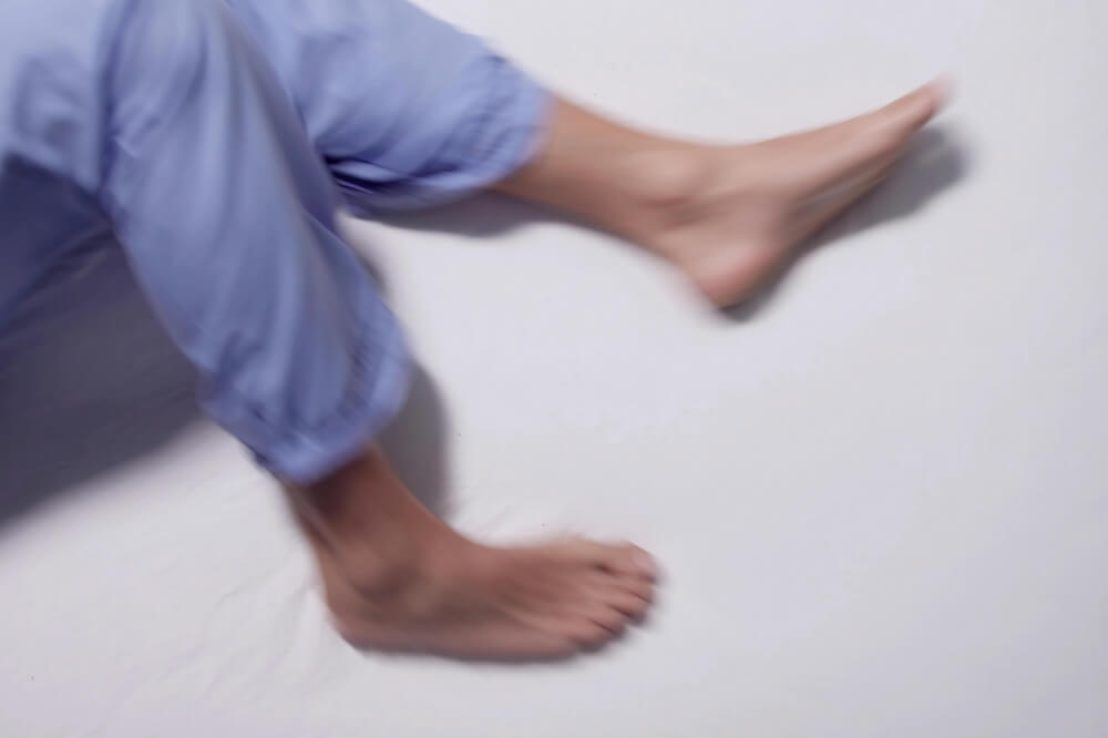 Person in light blue pants lying on their side with bare feet on a white examination table, possibly experiencing Restless Leg Syndrome symptoms or discomfort caused by varicose veins or spider veins, in Cleveland, Ohio.