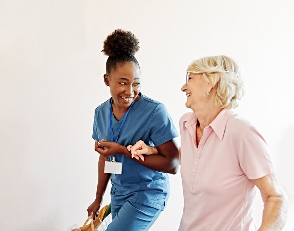 Nelson Vein Cleveland nurse in blue scrubs assisting senior woman post varicose vein treatment, indoor recovery support after procedure.