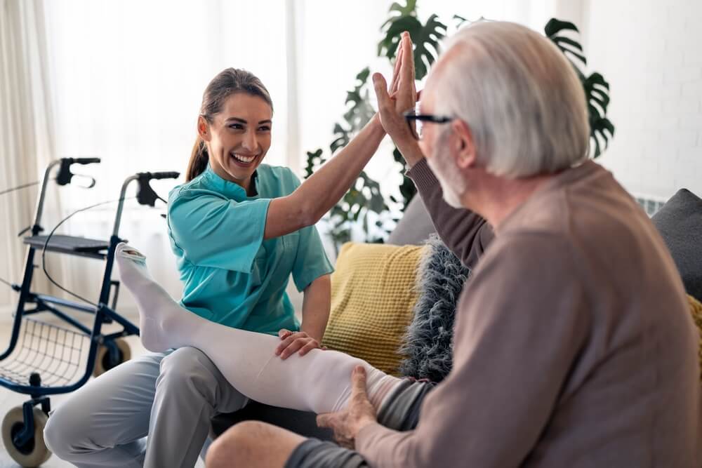 Nelson Vein Cleveland nurse assists senior man with compression therapy for varicose veins; walker visible in bright living room.