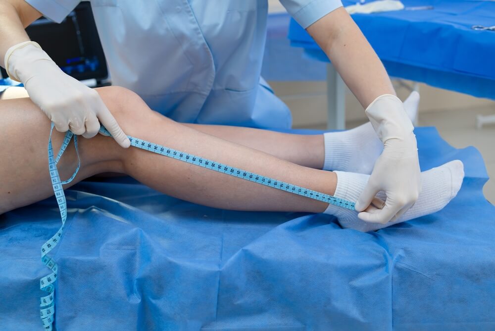 Nelson Vein Cleveland professional measuring lower leg for compression therapy, treating varicose veins; patient in white socks.