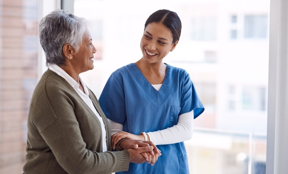 Nelson Vein Cleveland caregiver in blue scrubs supports elderly woman after varicose vein treatment, both smiling by window.