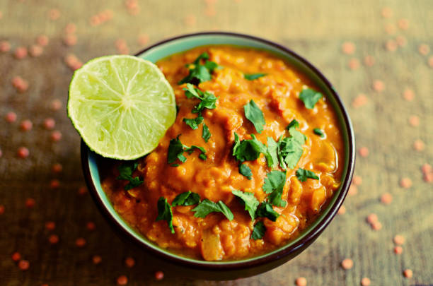 Red lentils dahl bowl with fresh lime and coriander leaves, wooden board